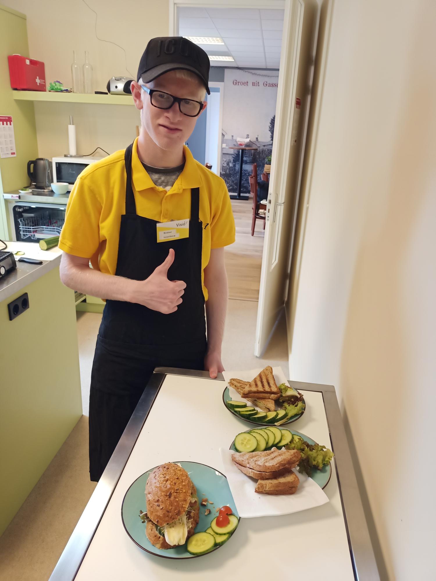 Leerling die bij Visit werkt, poseert lachend bij borden met belegde broodjes en steekt zijn duim op Leerling die bij Visit werkt, poseert lachend bij borden met belegde broodjes en steekt zijn duim op
