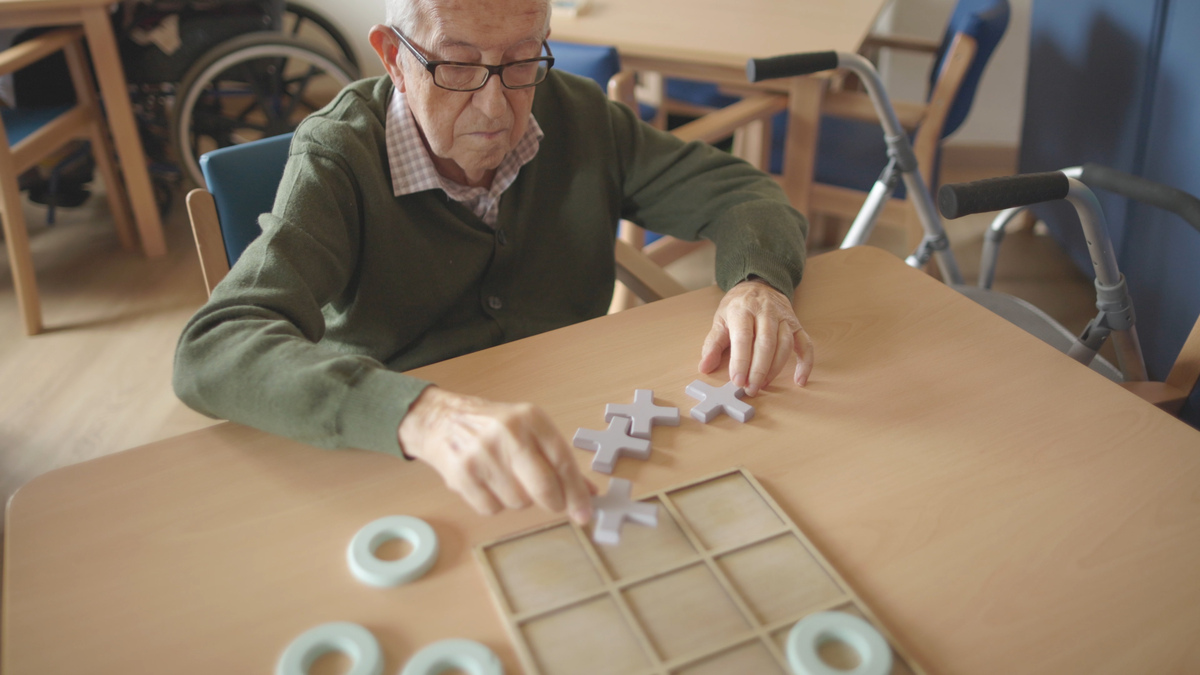 Oudere meneer speelt vergroot spel aan tafel Oudere meneer speelt vergroot spel aan tafel