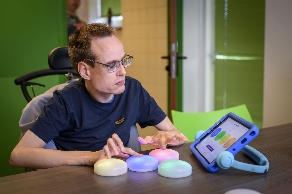 Cliënt met een visuele en verstandelijke beperking doet een tastspel met gekleurde lampen, dat gekoppeld is aan een iPad Cliënt met een visuele en verstandelijke beperking doet een tastspel met gekleurde lampen, dat gekoppeld is aan een iPad