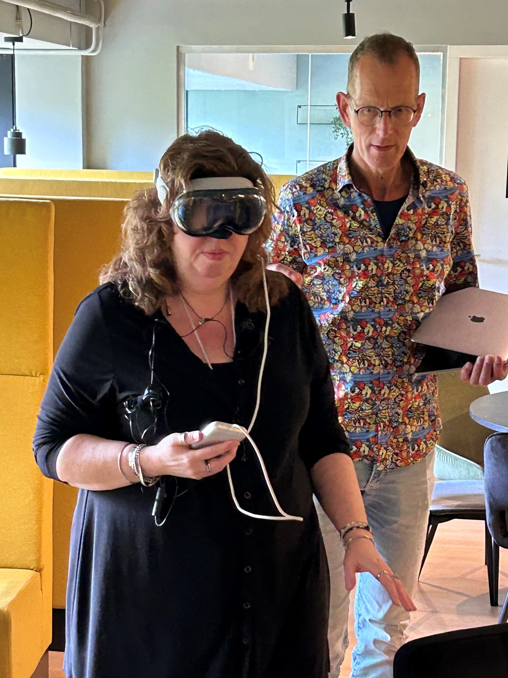 Een cliënt van Visio draagt een VR-bril. Ze is een app aan het testen. Achter haar staat iemand om haar te helpen. Een cliënt van Visio draagt een VR-bril. Ze is een app aan het testen. Achter haar staat iemand om haar te helpen.