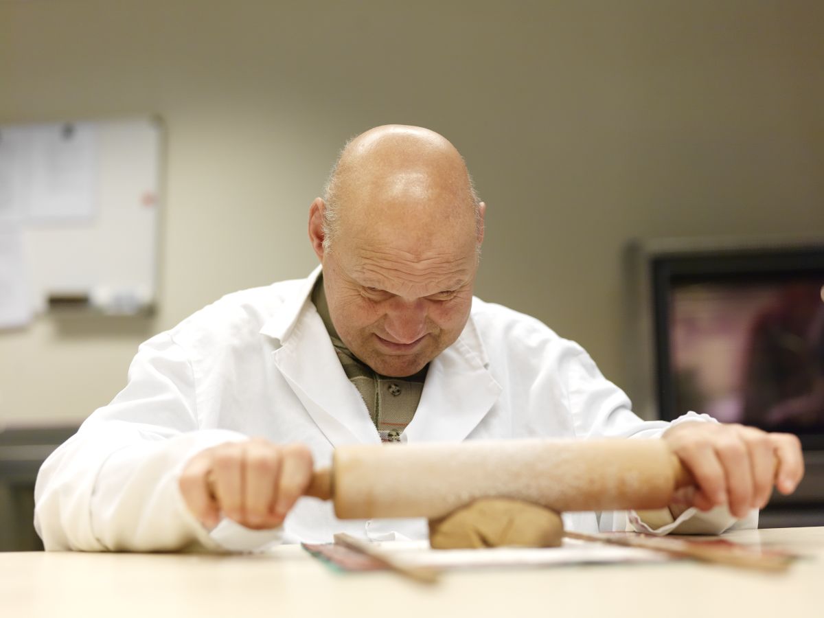 Man met een visuele en verstandelijke beperking rolt deeg uit Man met een visuele en verstandelijke beperking rolt deeg uit