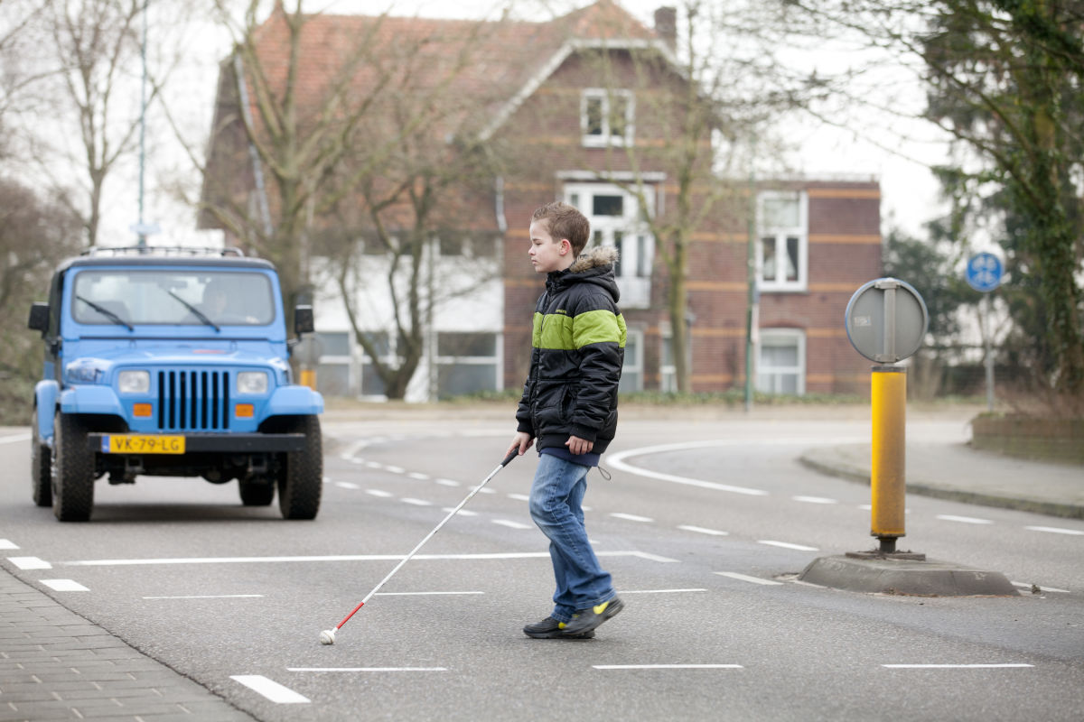 Jonge jongen steekt openbare weg over met behulp van taststok