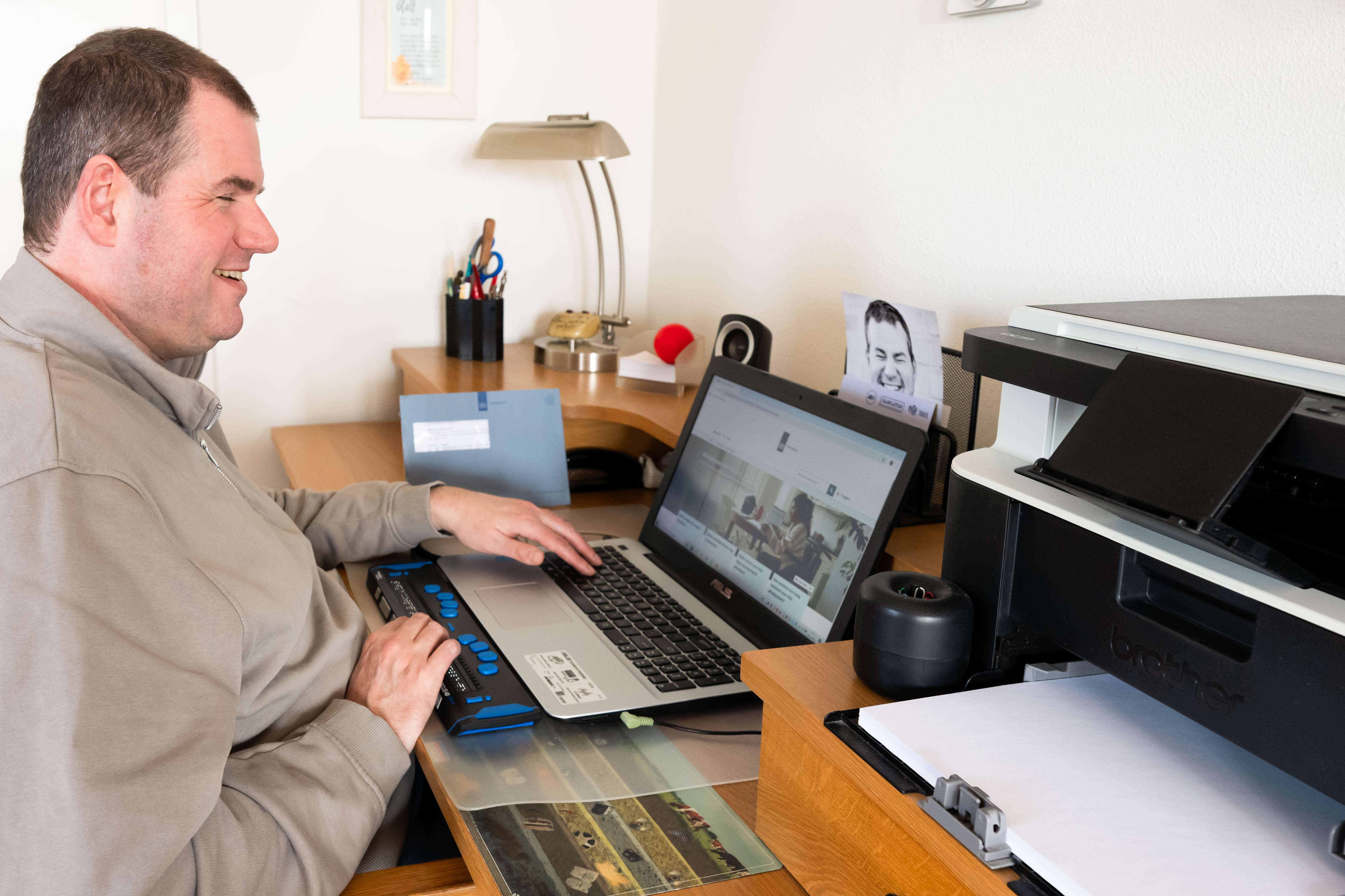 Ralf zit achter zijn laptop aan een bureau. Hij lacht. Ralf zit achter zijn laptop aan een bureau. Hij lacht.