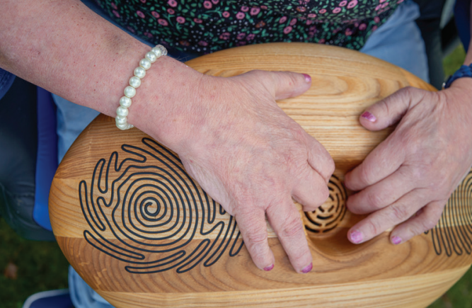 Twee handen houden de CRDL vast. Het is een houten ovaal met gegrafeerde lijnen erop. Twee handen houden de CRDL vast. Het is een houten ovaal met gegrafeerde lijnen erop.