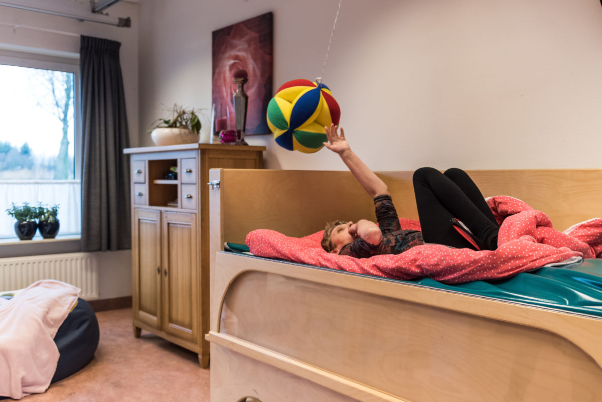 Cliënt speelt met een zachte bal terwijl zij op een bed ligt Cliënt speelt met een zachte bal terwijl zij op een bed ligt