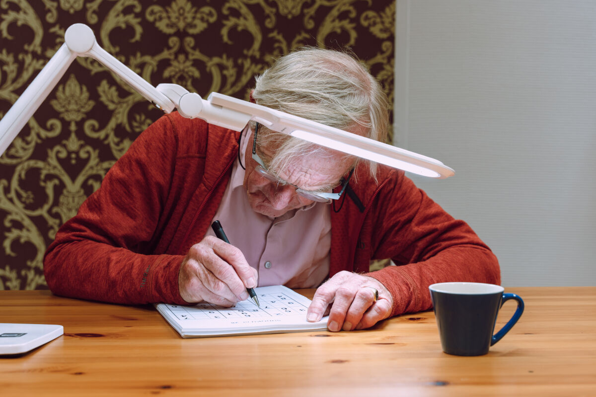 Slechtziende man gebruikt speciale leesbril met leeslamp Slechtziende man gebruikt speciale leesbril met leeslamp