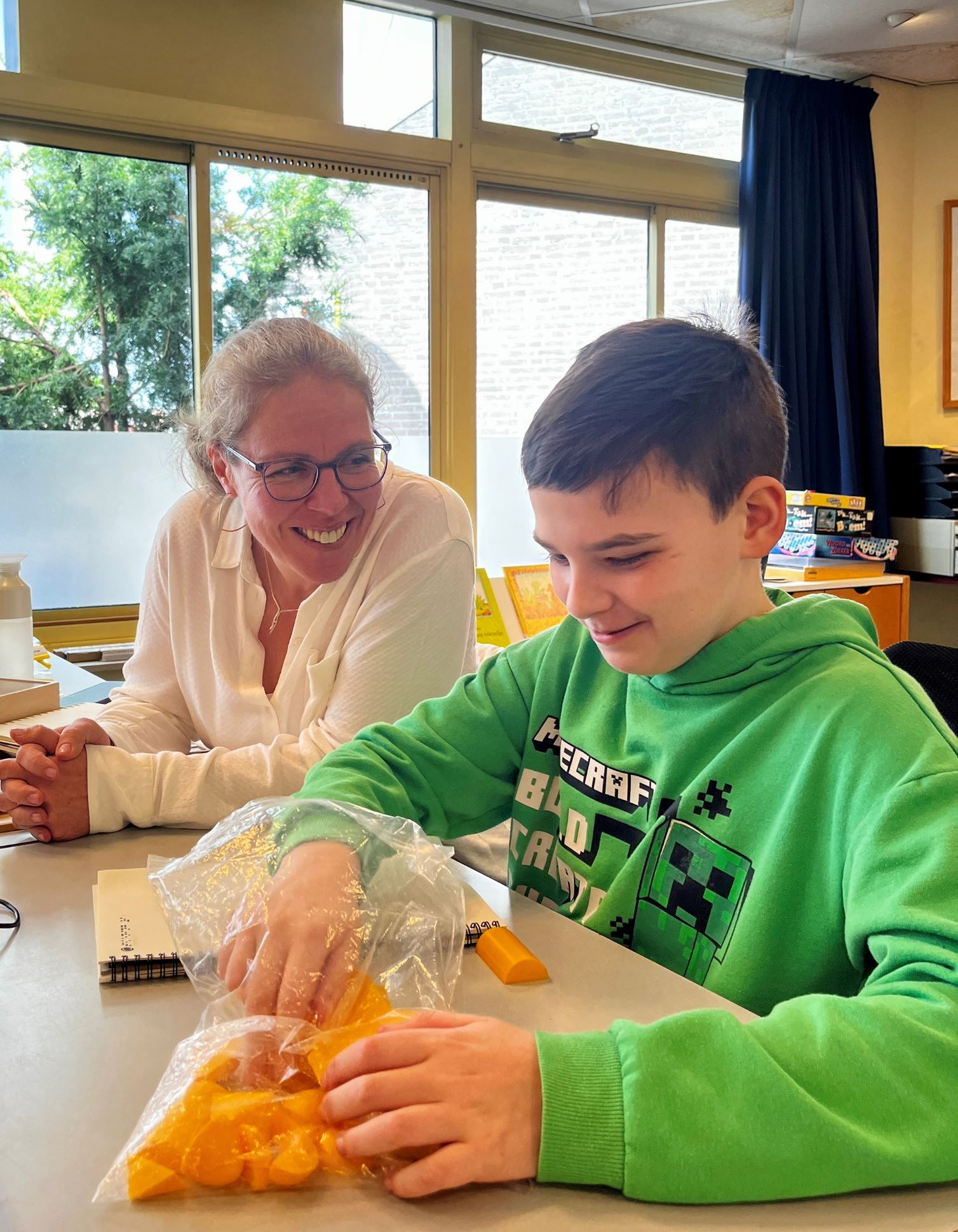 Dean met ambulant onderwijskundig begeleider van Visio aan tafel in een klaslokaal Dean met ambulant onderwijskundig begeleider van Visio aan tafel in een klaslokaal
