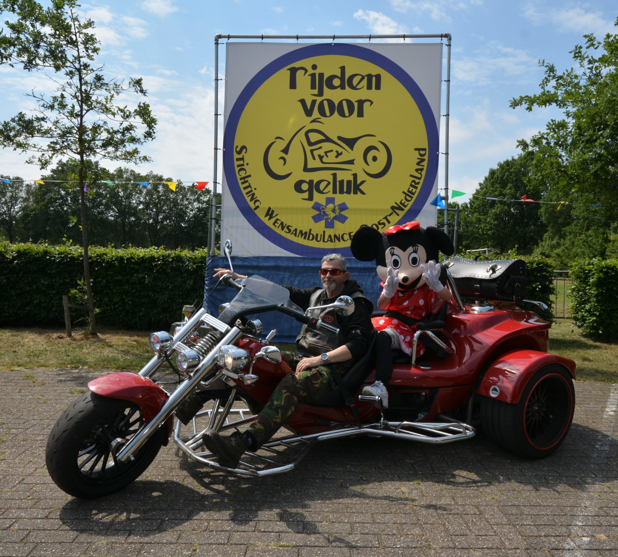 Ruud en Carla poseren lachend op de trike tijdens de motortocht Rijden voor geluk waarbij Carla achterop zit en is verkleed als Mini Mouse