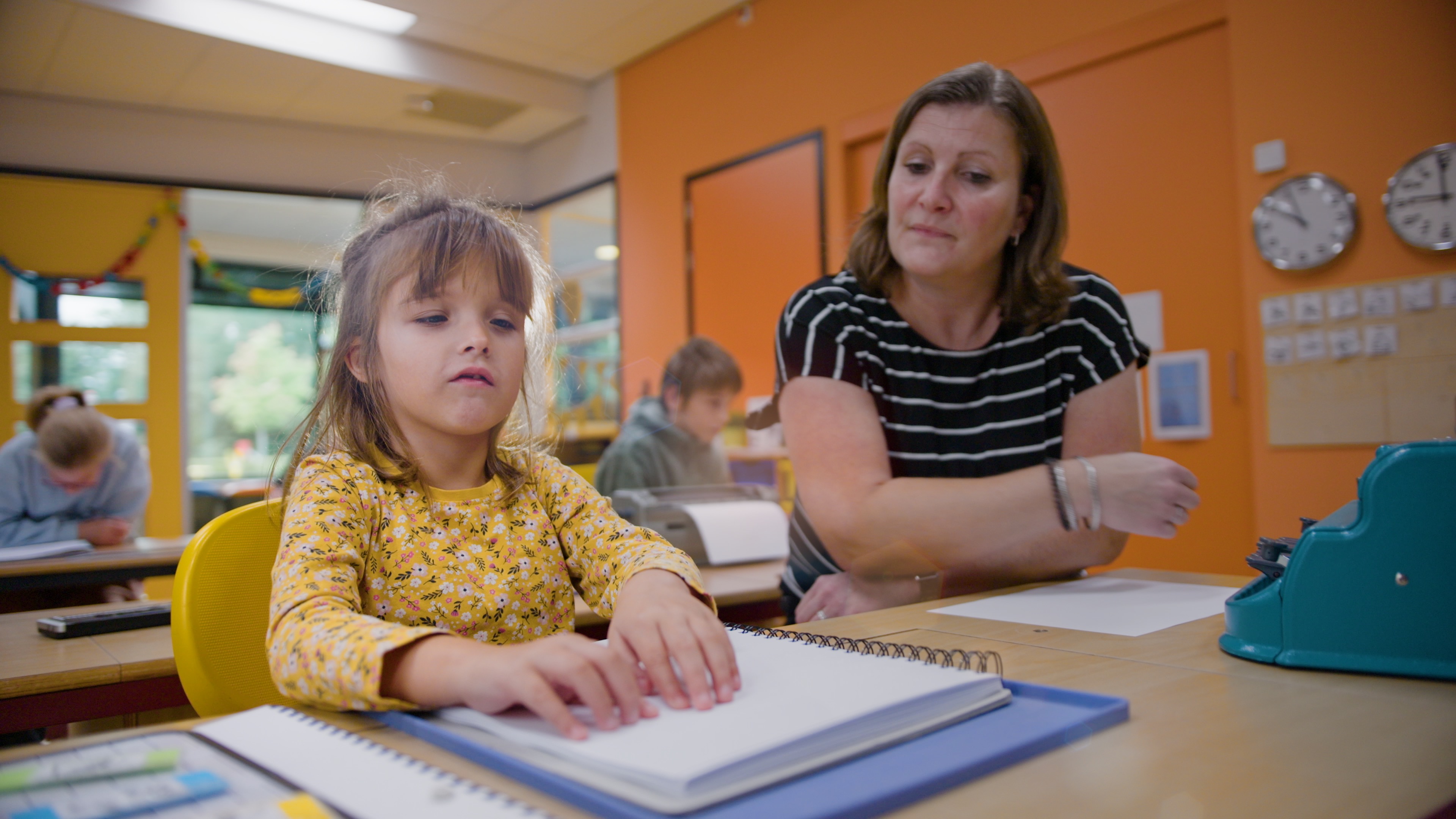 Elena zit in de klas naast de juf. Ze is braille aan het lezen. Elena zit in de klas naast de juf. Ze is braille aan het lezen.