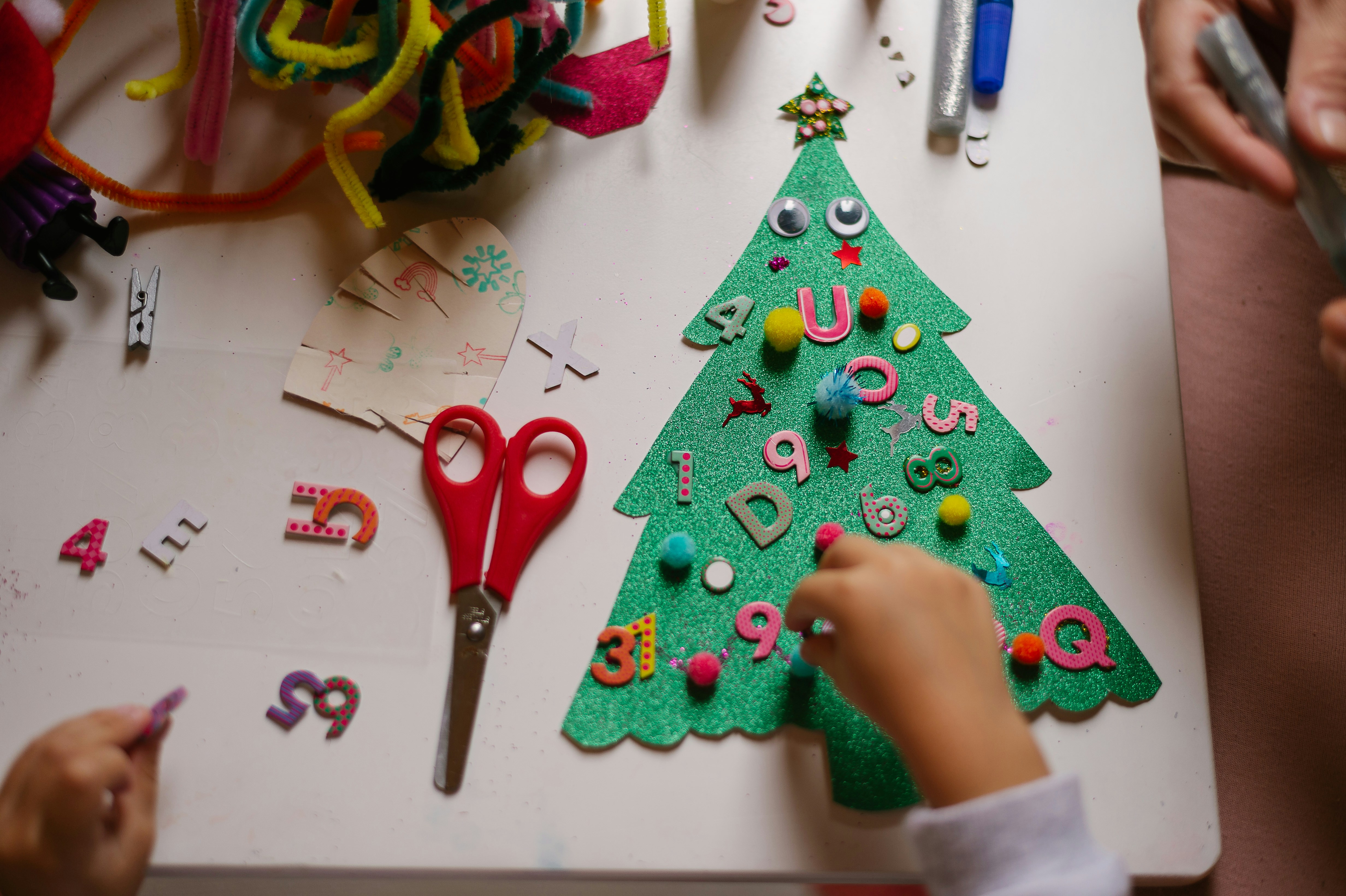 Kind beplakt een kerstboom van glitterkarton met voelbare items zoals pluizige bolletjes, oogjes en dikke cijfers en letters