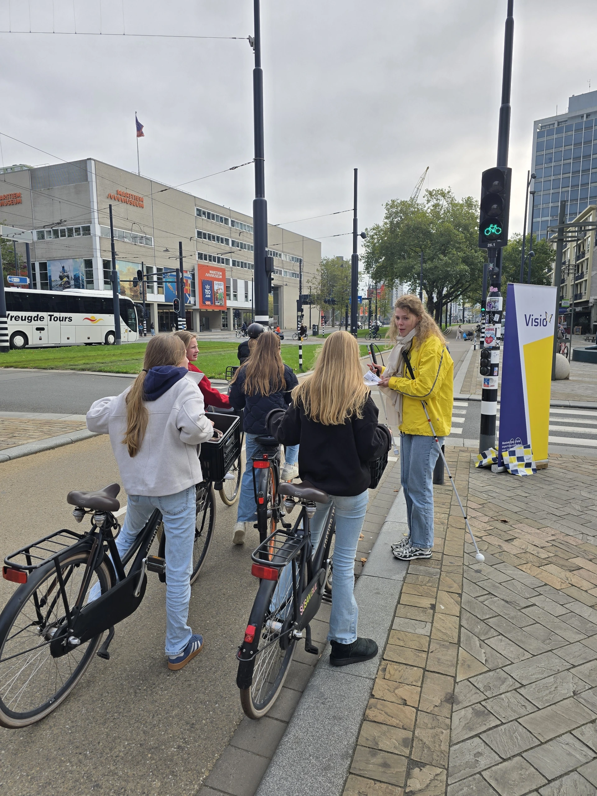 Medewerker van Visio attendeert fietser op de Coolsingel in Rotterdam op het verkeersteken met de witte stok