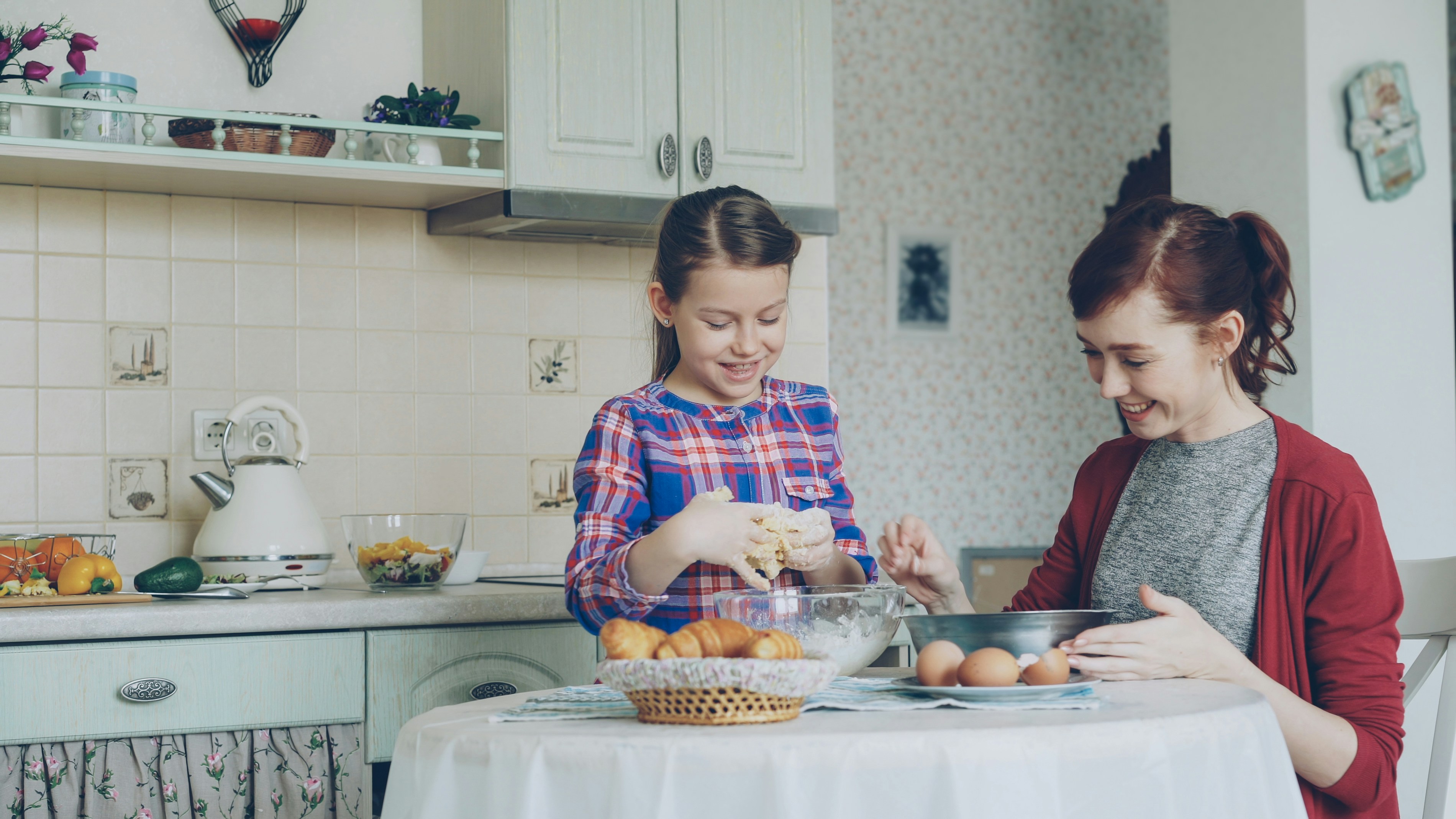 moeder en kind bakken samen koekjes in de keuken, het meisje kneed het deeg en de moeder breekt de eieren