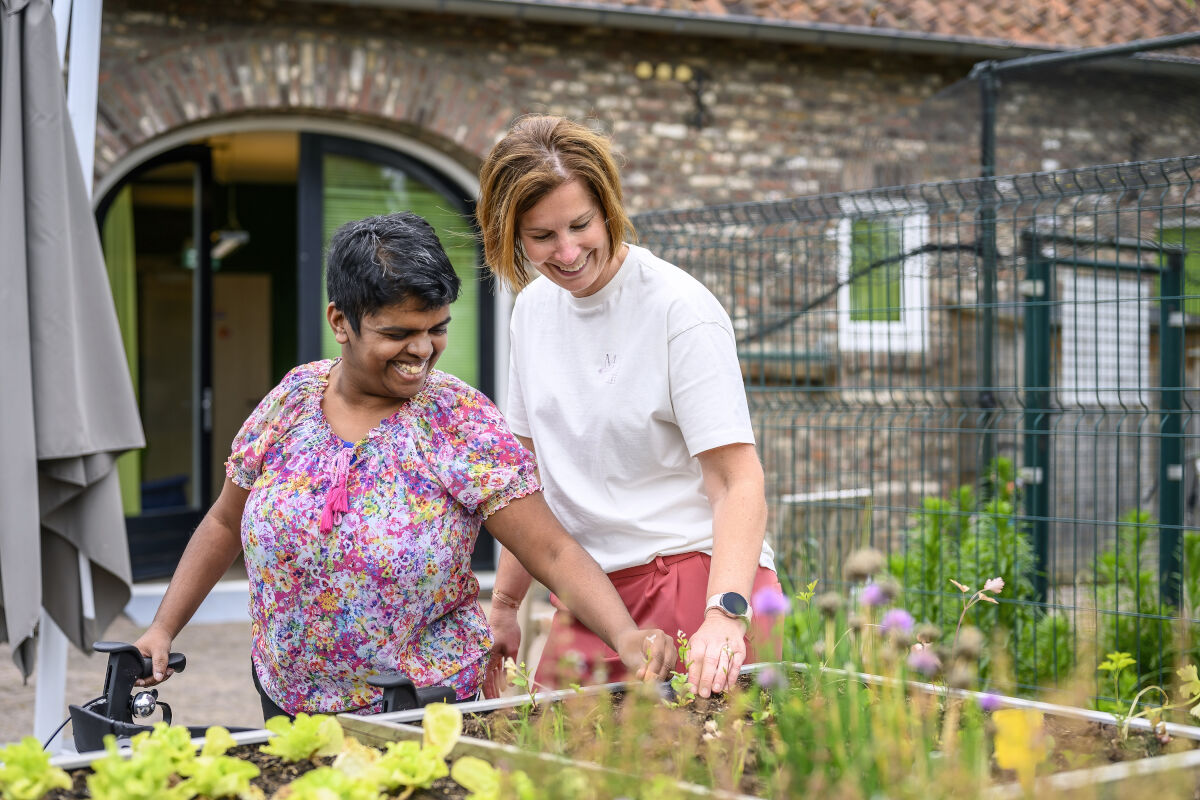 Vrouwelijke cliënt met rollator en een medewerker werken samen bij een verhoogde moestuinbak Vrouwelijke cliënt met rollator en een medewerker werken samen bij een verhoogde moestuinbak