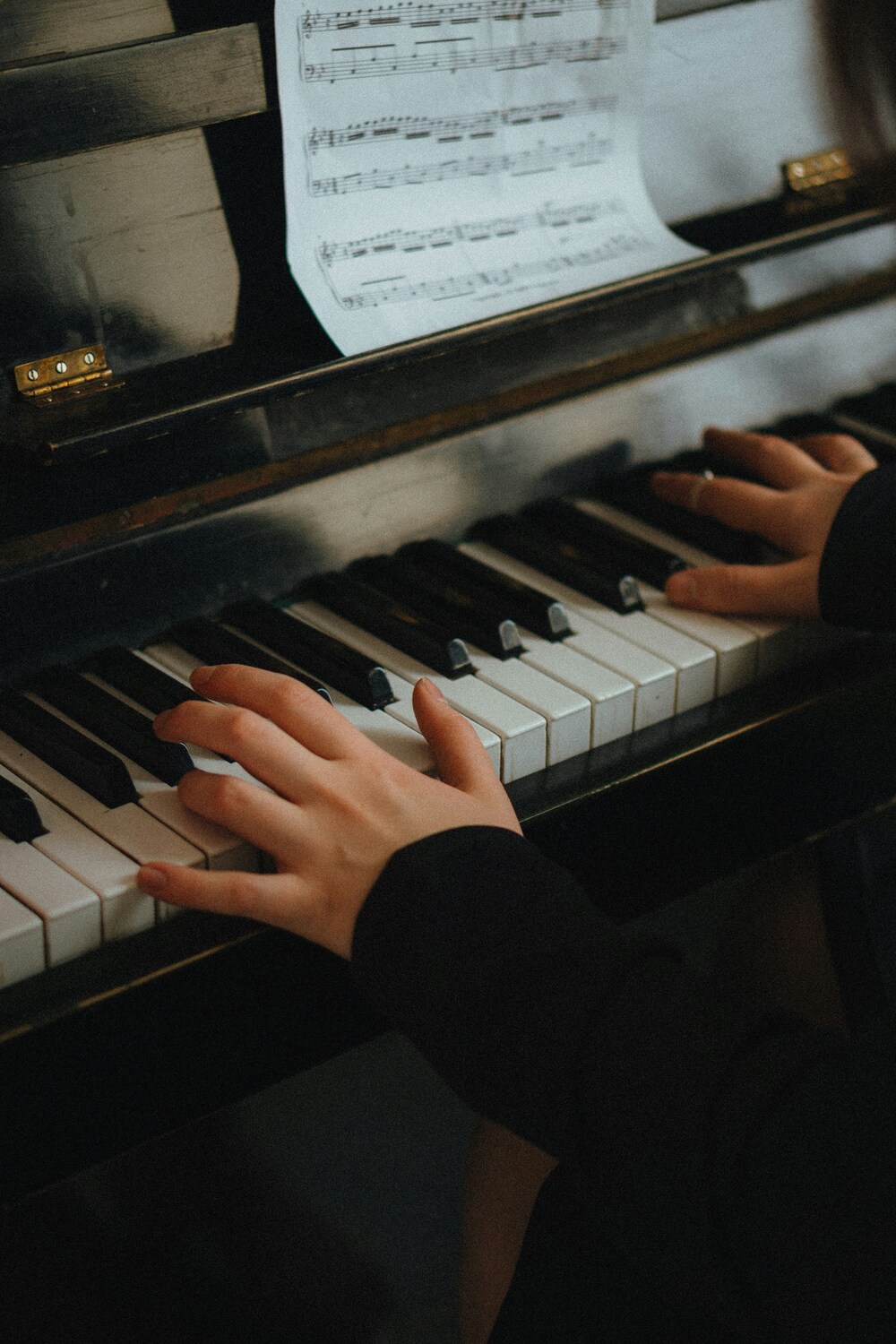 Dame speelt piano, je zien alleen haar handen op de toetsen en een stukje van de bladmuziek Dame speelt piano, je zien alleen haar handen op de toetsen en een stukje van de bladmuziek
