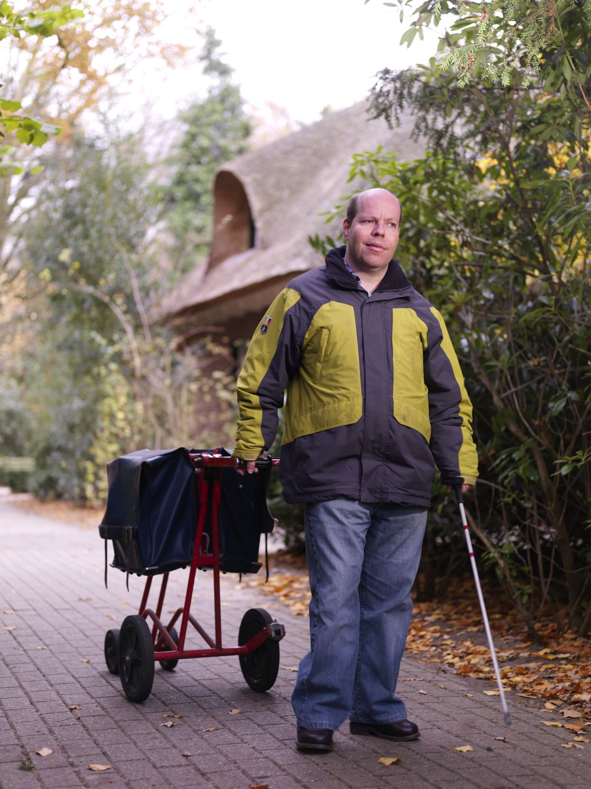Cliënt brengt de post rond met een taststok in zijn hand en aan zijn andere hand een postwagentje Cliënt brengt de post rond met een taststok in zijn hand en aan zijn andere hand een postwagentje