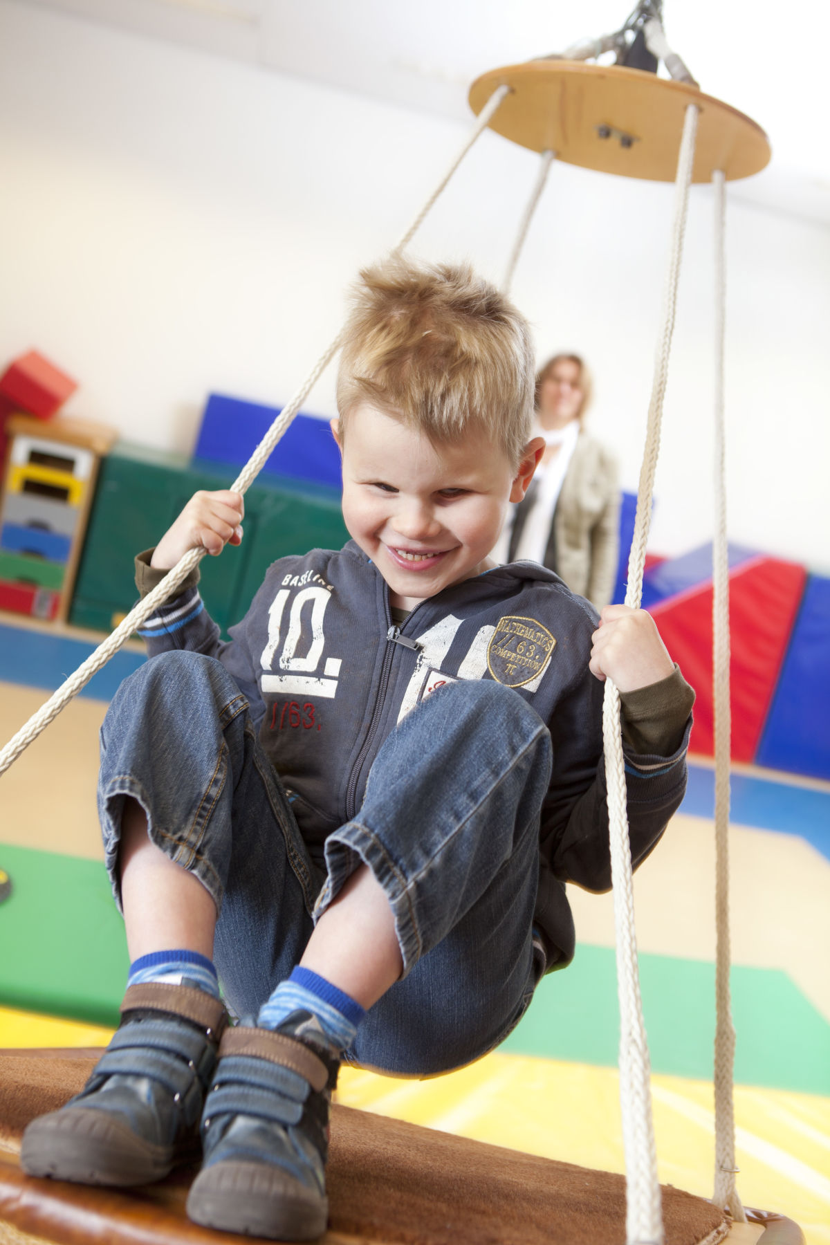 Een jongetje zit op een schommel. In de achtergrond zijn kleurrijke matten te zien. Een jongetje zit op een schommel. In de achtergrond zijn kleurrijke matten te zien.
