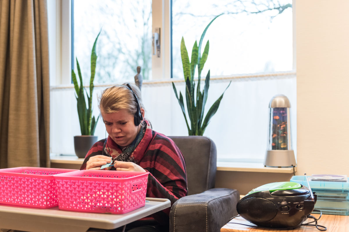 Cliënt zit in stoel en luister muziek met een koptelefoon Cliënt zit in stoel en luister muziek met een koptelefoon