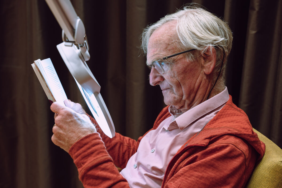Man met visuele beperking leest met speciale leeslamp Man met visuele beperking leest met speciale leeslamp