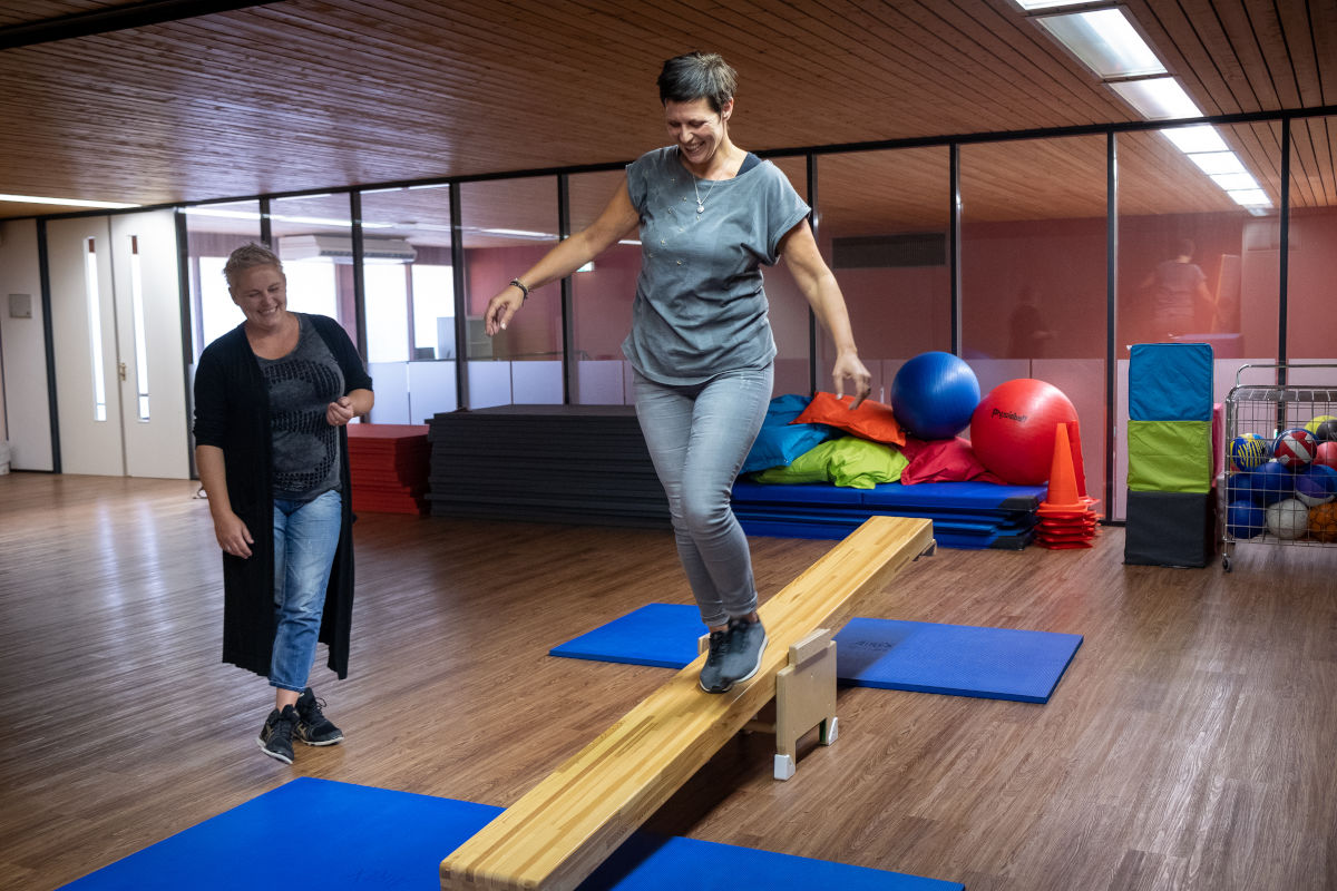 Cliënt van Visio Het Loo Erf voert bewegingsoefeningen uit in een sportzaal onder begeleiding van een medewerker Cliënt van Visio Het Loo Erf voert bewegingsoefeningen uit in een sportzaal onder begeleiding van een medewerker