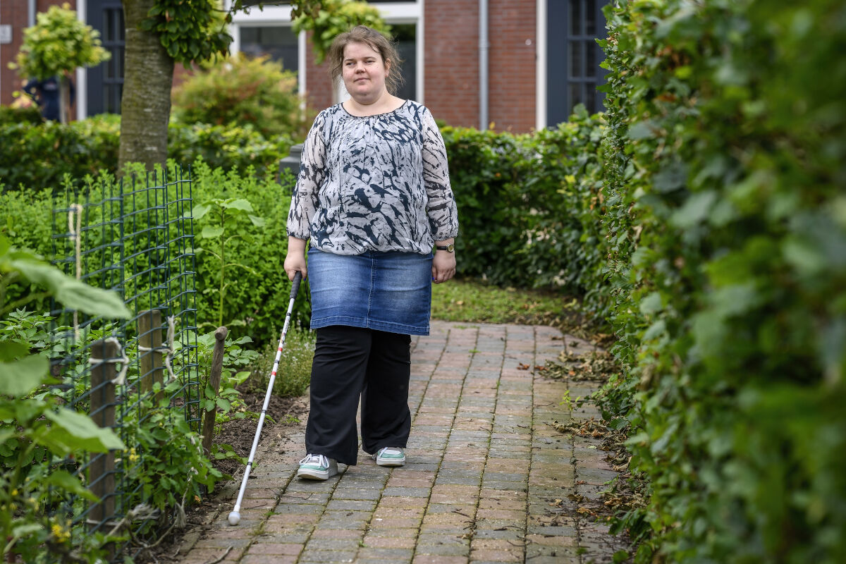 Dame met taststok loopt buiten op een stoepje bij Visio Wonen & Dagbesteding Stramproy Dame met taststok loopt buiten op een stoepje bij Visio Wonen & Dagbesteding Stramproy