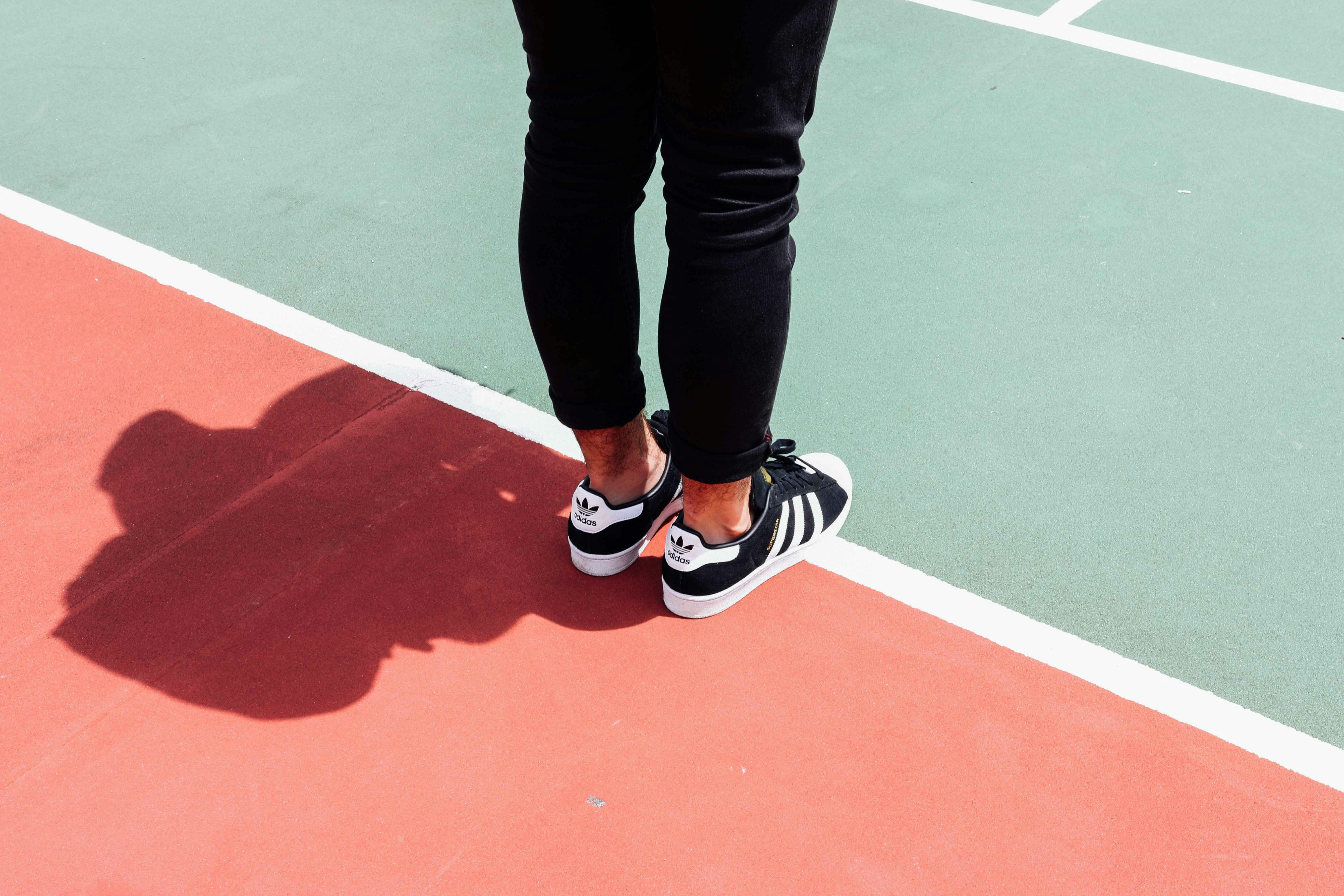 Iemand staat op een lijn op een sportveld en draagt sportschoenen, je ziet alleen de knieën tot en met de voeten