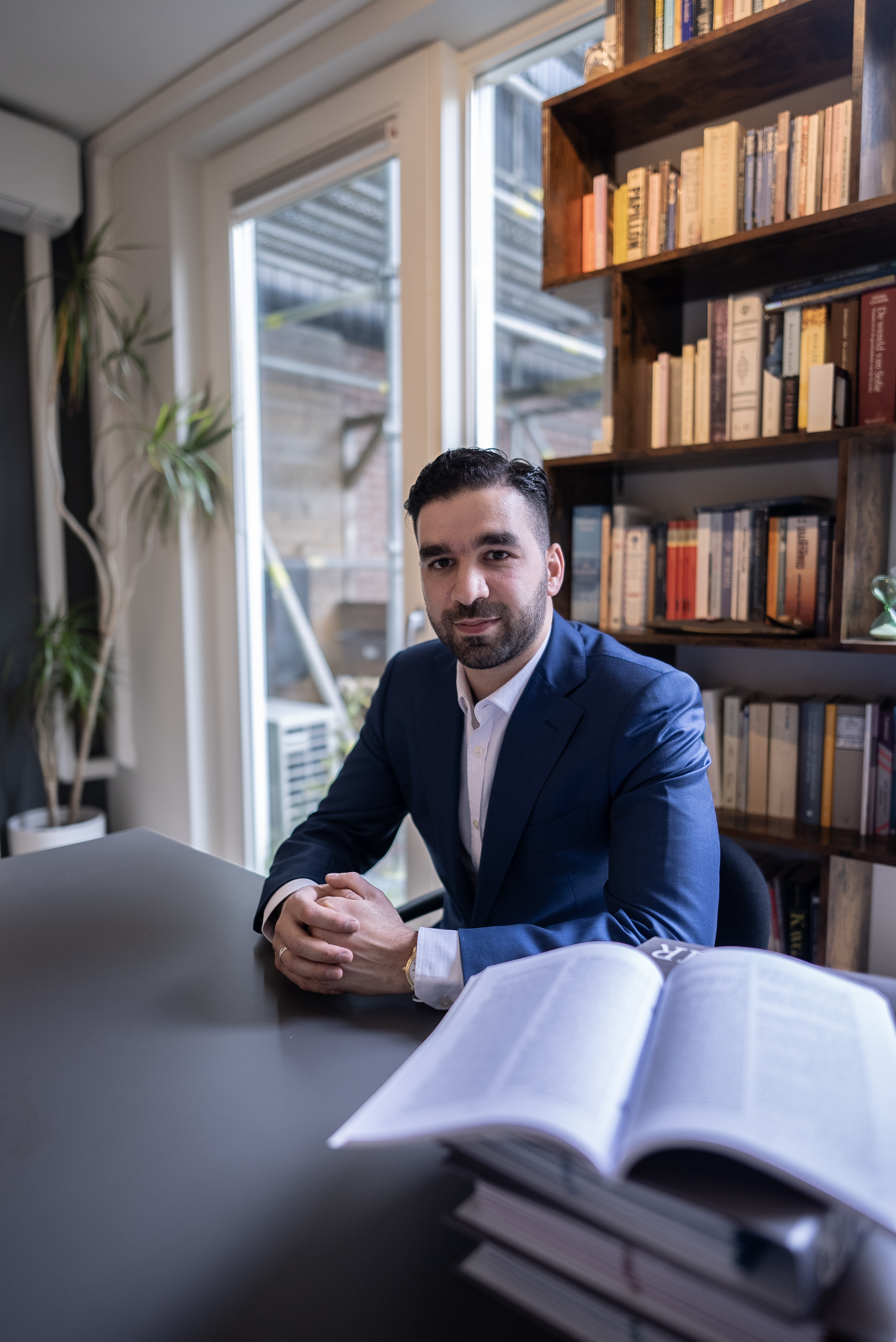 Foto van Faruk, hij zit aan een bureau in een kantoor met een blauw pak aan. Foto van Faruk, hij zit aan een bureau in een kantoor met een blauw pak aan.