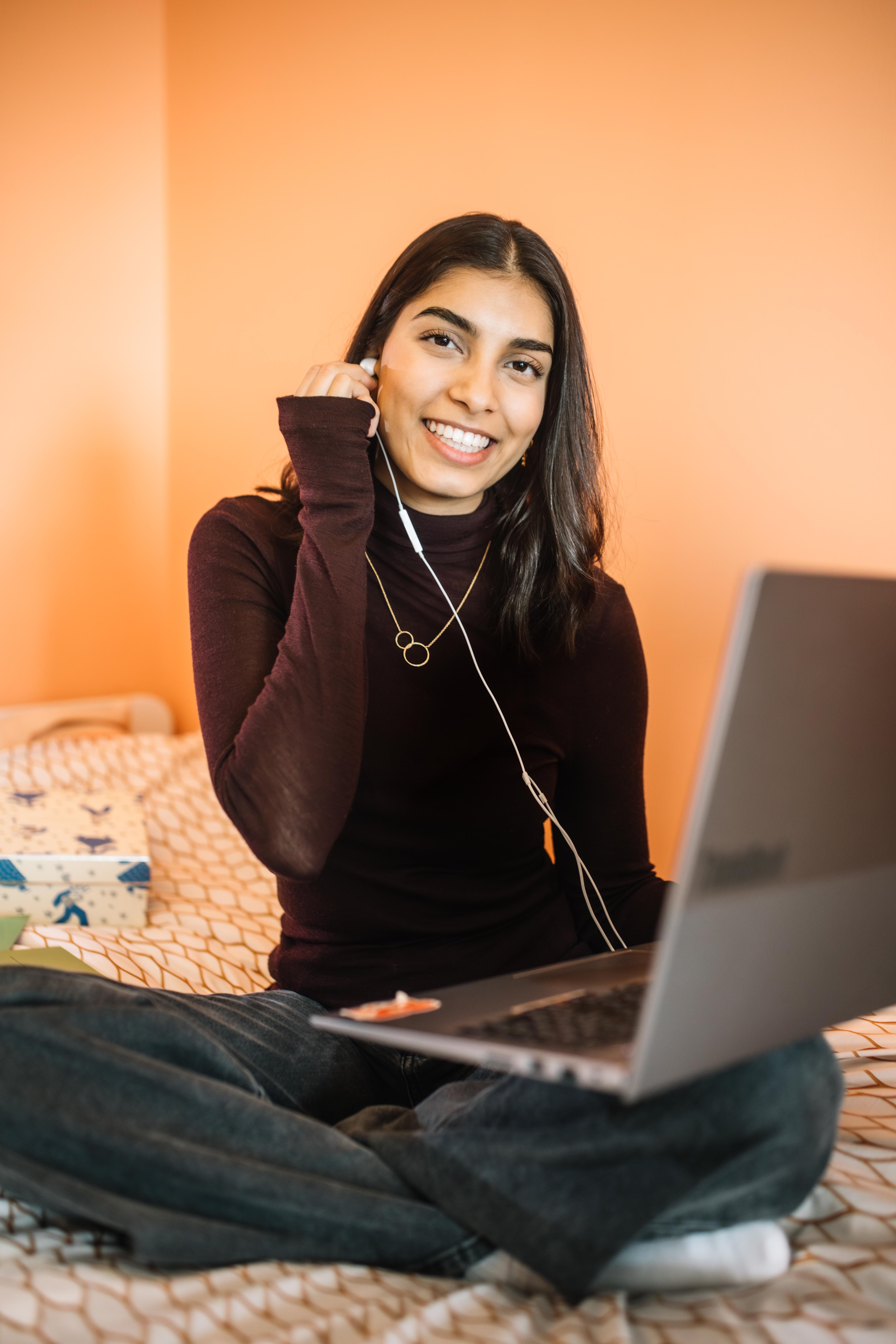 Bodhi zit op haar bed met haar laptop. Ze doet een oordopje, aangesloten aan haar laptop, in haar oor. Bodhi zit op haar bed met haar laptop. Ze doet een oordopje, aangesloten aan haar laptop, in haar oor.