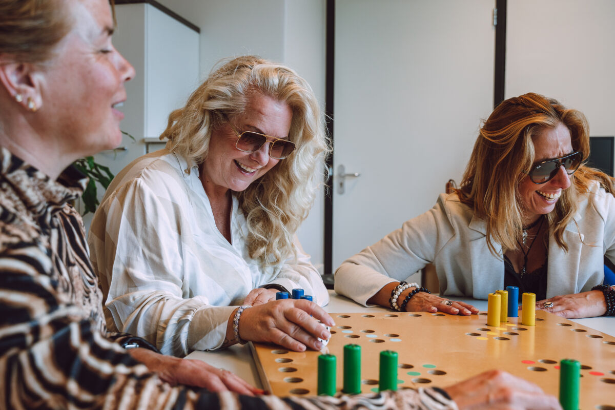 Drie vrouwen spelen samen een tactiele versie van Mens erger je niet. Drie vrouwen spelen samen een tactiele versie van Mens erger je niet.