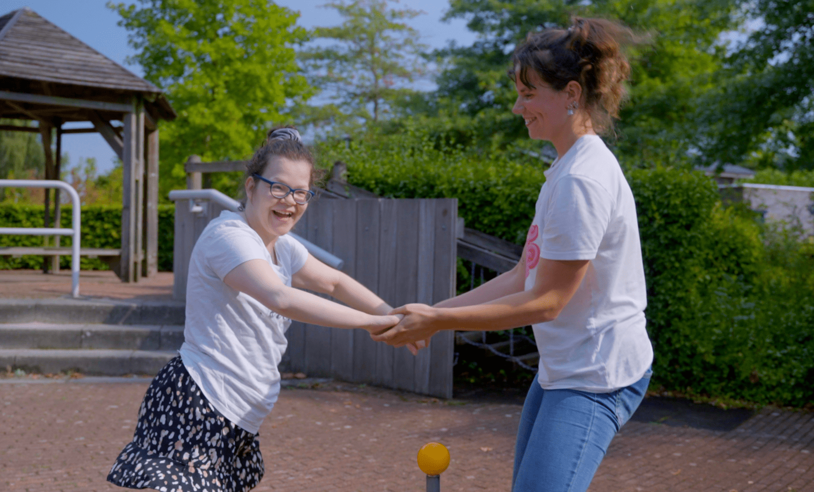 Cliënt met een visuele en verstandelijke beperking en haar begeleider draaien rondjes op een speeltoestel Cliënt met een visuele en verstandelijke beperking en haar begeleider draaien rondjes op een speeltoestel