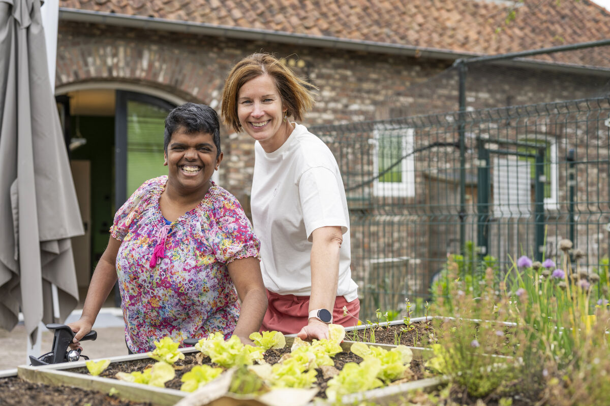 Cliënt en medewerker van Visio poseren glimlachend bij een moestuin Cliënt en medewerker van Visio poseren glimlachend bij een moestuin