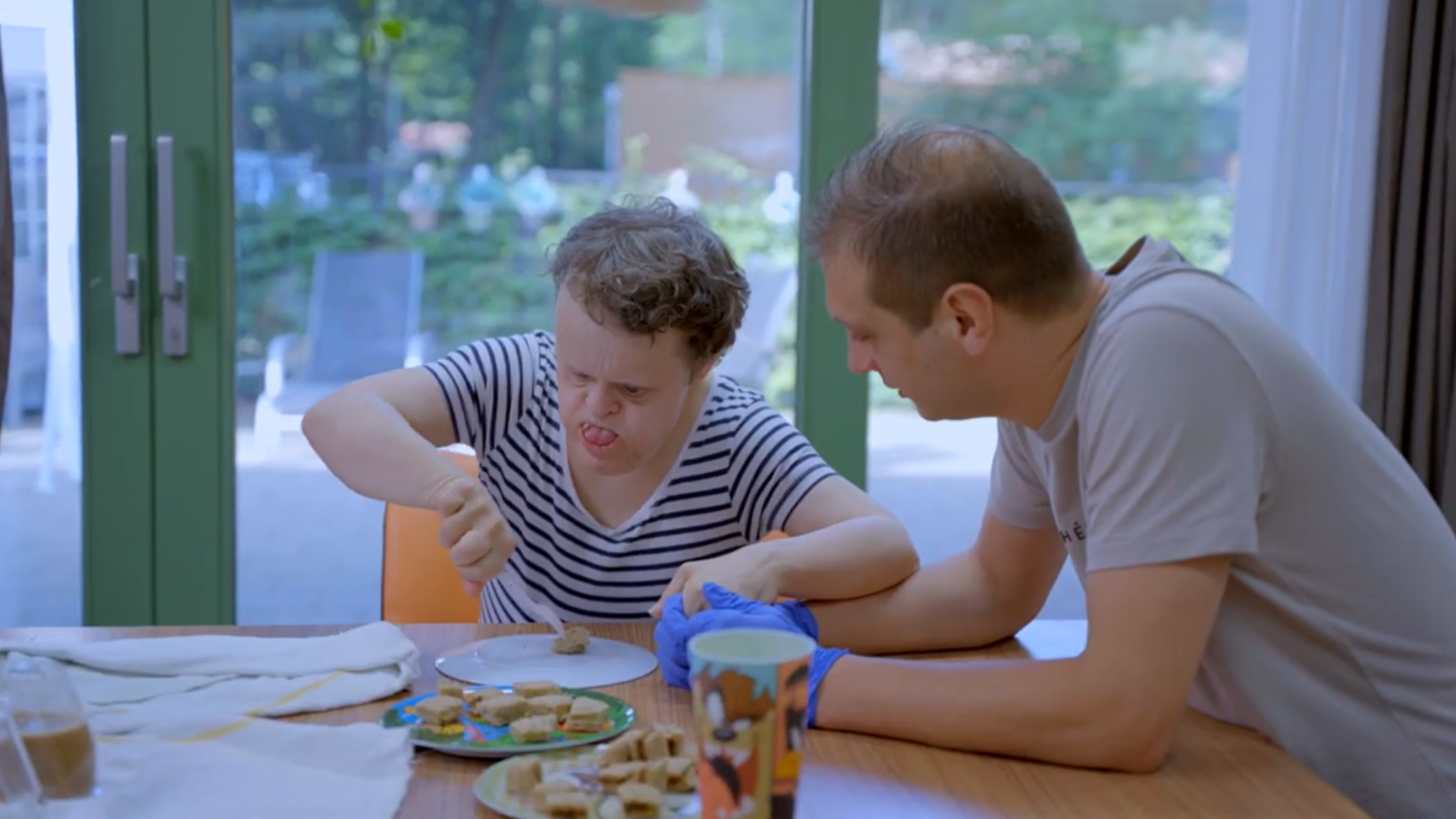 Cliënt en begeleider zitten samen aan tafel, de cliënt eet een boterham Cliënt en begeleider zitten samen aan tafel, de cliënt eet een boterham