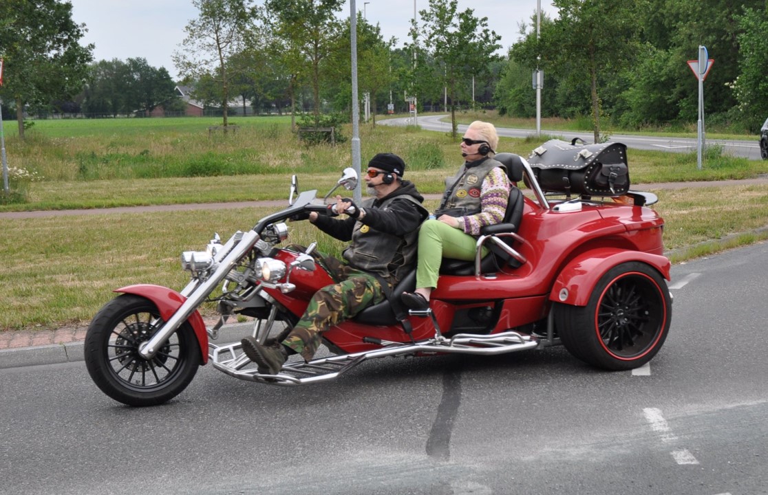 Carla zit achterop een rode trike en haar partner Ruud bestuurt de trike - een motor met drie wielen