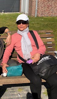 Maureen zit op een bankje in de zon. Ze draagt een pet en een zonnebril. Maureen zit op een bankje in de zon. Ze draagt een pet en een zonnebril.