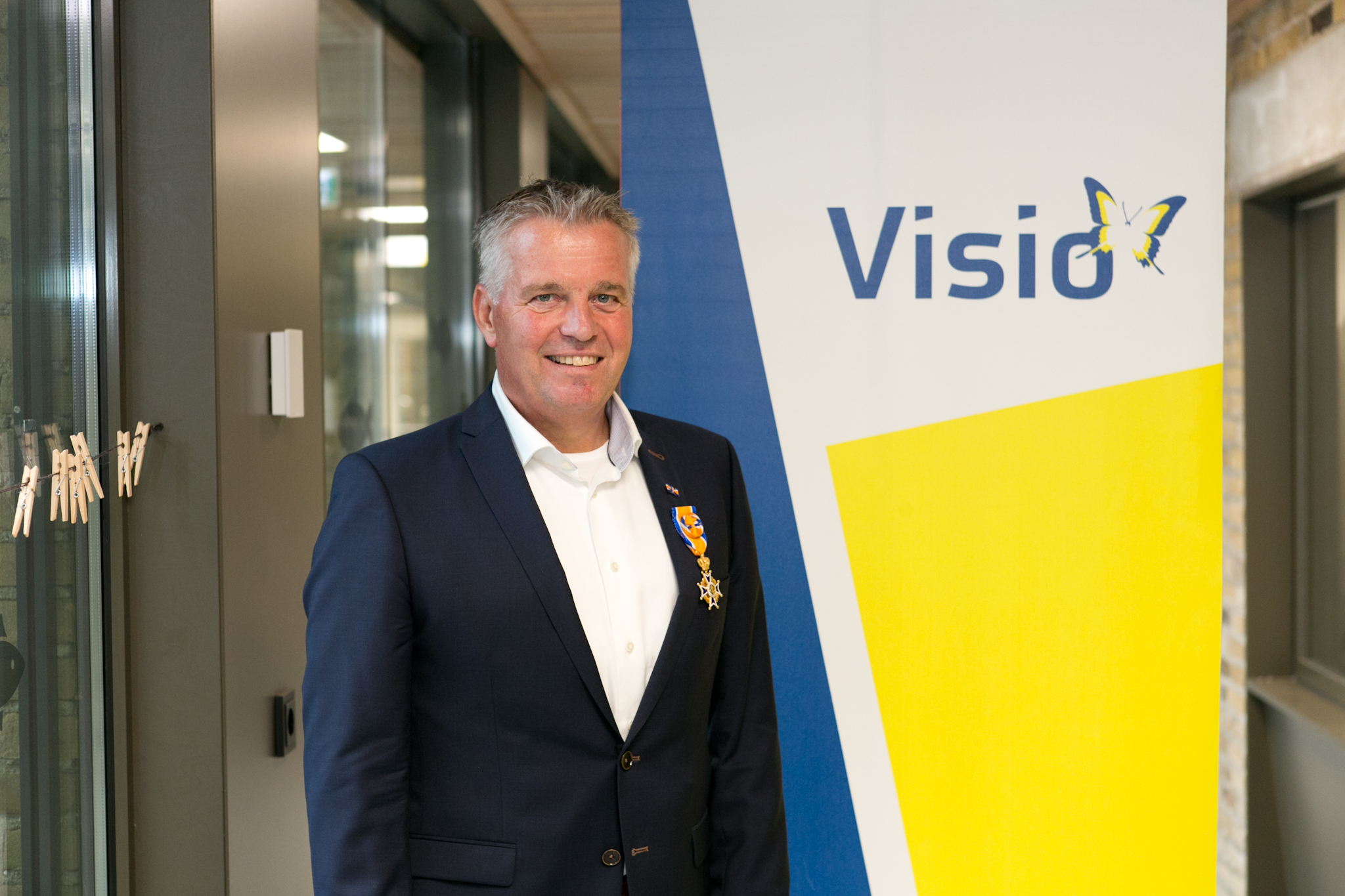 Portretfoto van Michiel Janssen, directeur Visio Onderwijs, hij poseert voor een banner met het Visio-logo