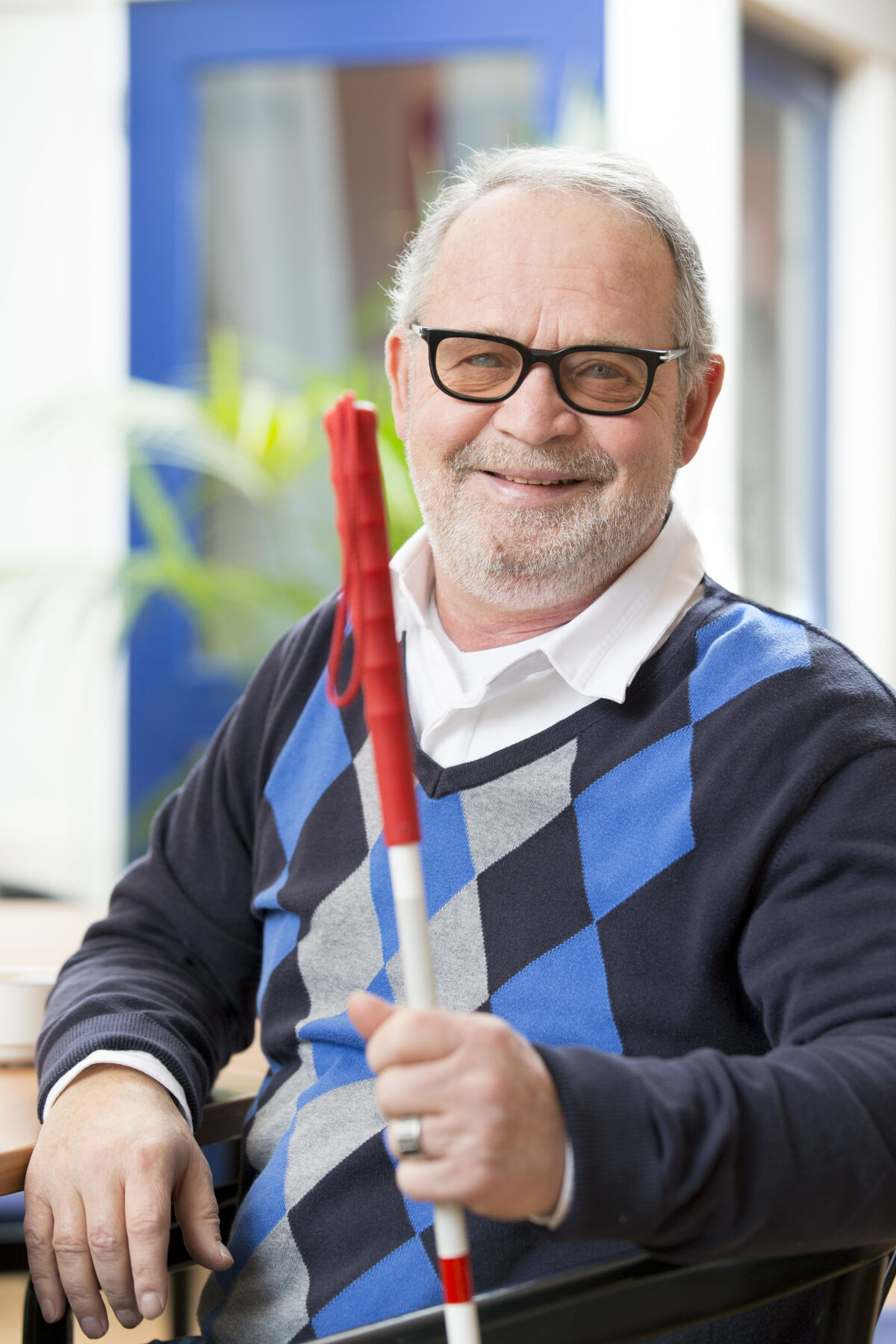 Oudere man met glaucoom glimlacht zittend met een taststok in zijn hand Oudere man met glaucoom glimlacht zittend met een taststok in zijn hand