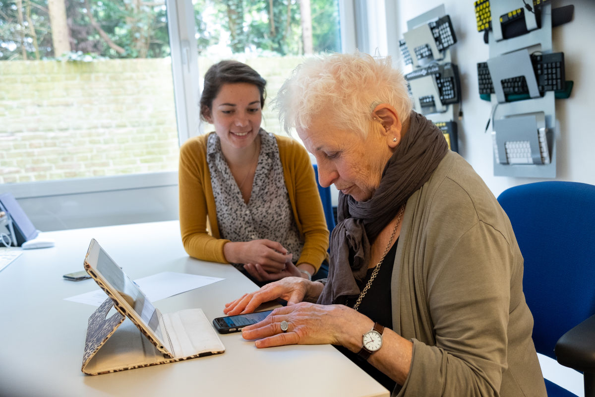 Oudere mevrouw krijgt ondersteuning in het gebruiken van haar telefoon en iPad. Oudere mevrouw krijgt ondersteuning in het gebruiken van haar telefoon en iPad.
